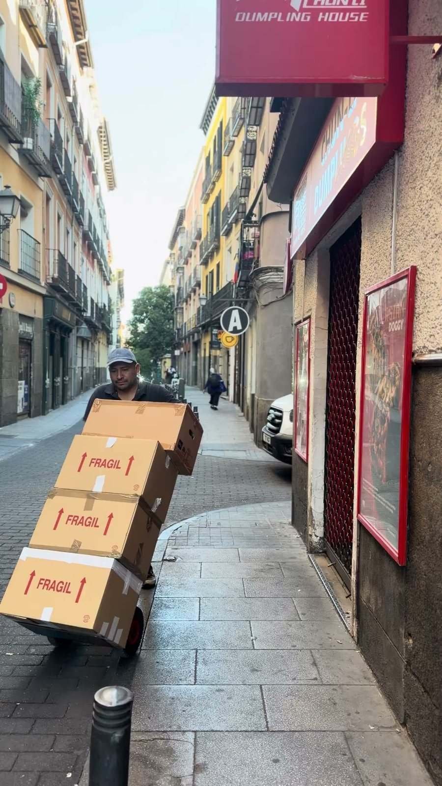 A mover pushes a hand truck with five boxes marked fragile down a narrow street