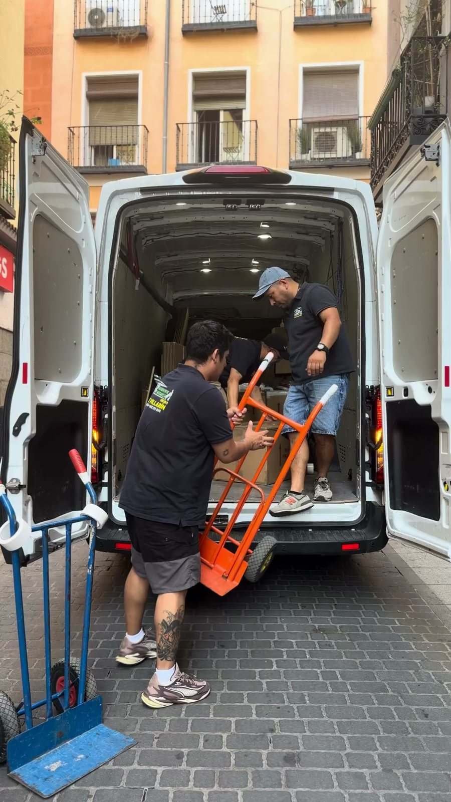 Pérez Villarín movers take hand trucks back to the open van parked in front of a building