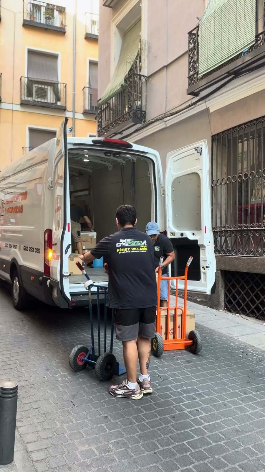 Furgoneta aparcada en una calle estrecha mientras dos operarios llevan carretillas