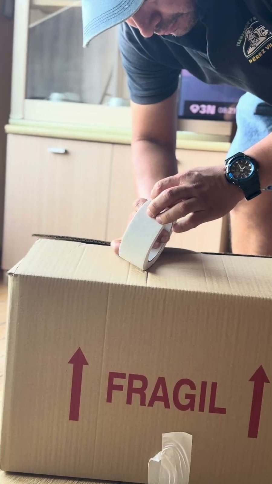 Manos precintando una caja de cartón marcada como frágil